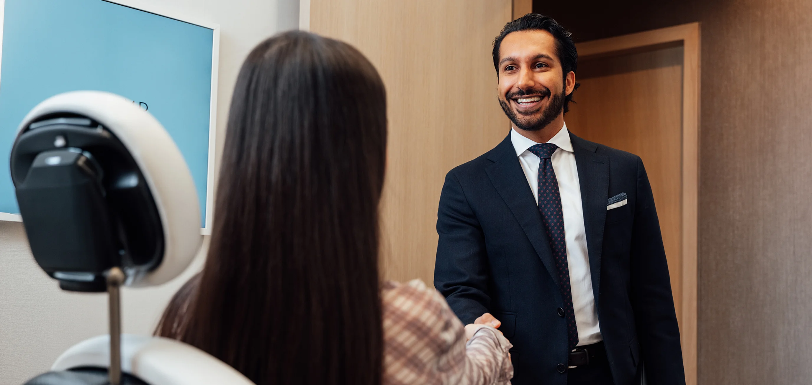 Dr Sameer Halani in suit greeting woman with handshake in modern office lobby - in New York , NY