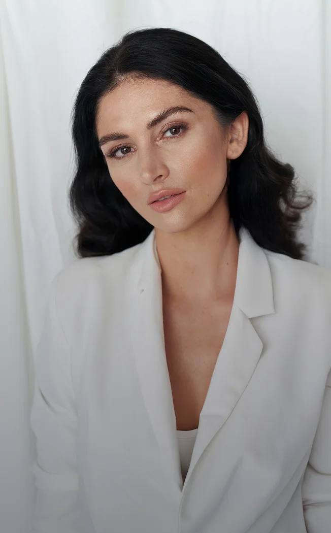 Professional woman in white blazer with dark hair looking at camera against neutral background - Eyes in New York , NY