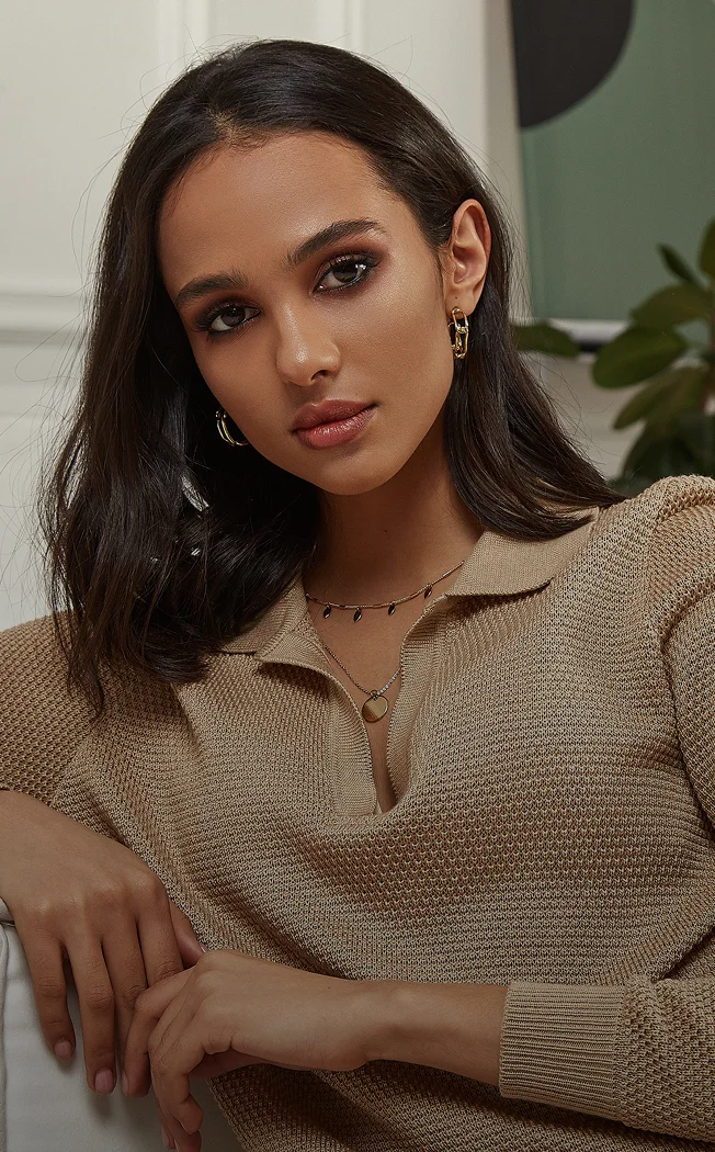 Woman in beige collared shirt with dark hair and hoop earrings posing indoors with plant in background - non surgical in New York , NY