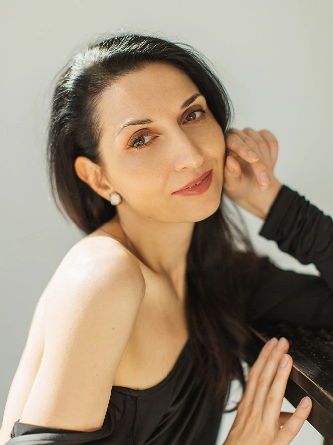 Woman with long dark hair in black top posing with hand near face against white background - chemical peels in New York , NY