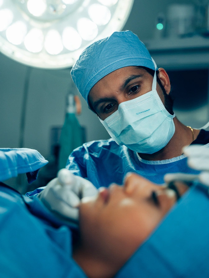 Dr Sameer Halani MD in blue scrubs and mask performing procedure on patient in operating room - chin augmentation in New York , NY