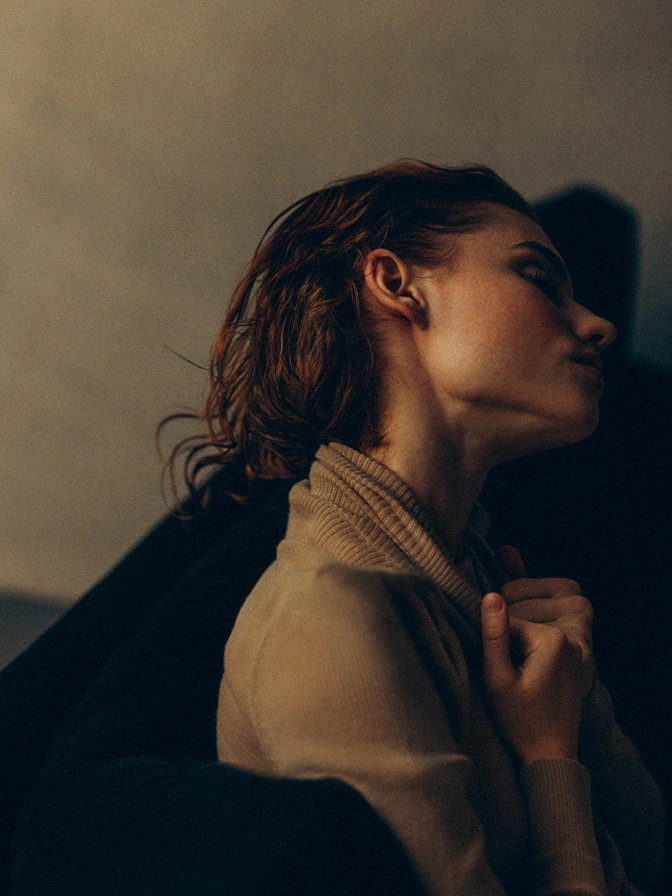 Woman in profile wearing beige turtleneck sweater against neutral background with dramatic shadow lighting - otoplasty in New York , NY