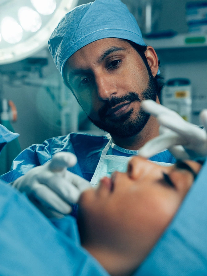 Dr Sameer Halani MD in blue scrubs and surgical cap performing medical procedure in operating room - rhinoplasty in New York , NY
